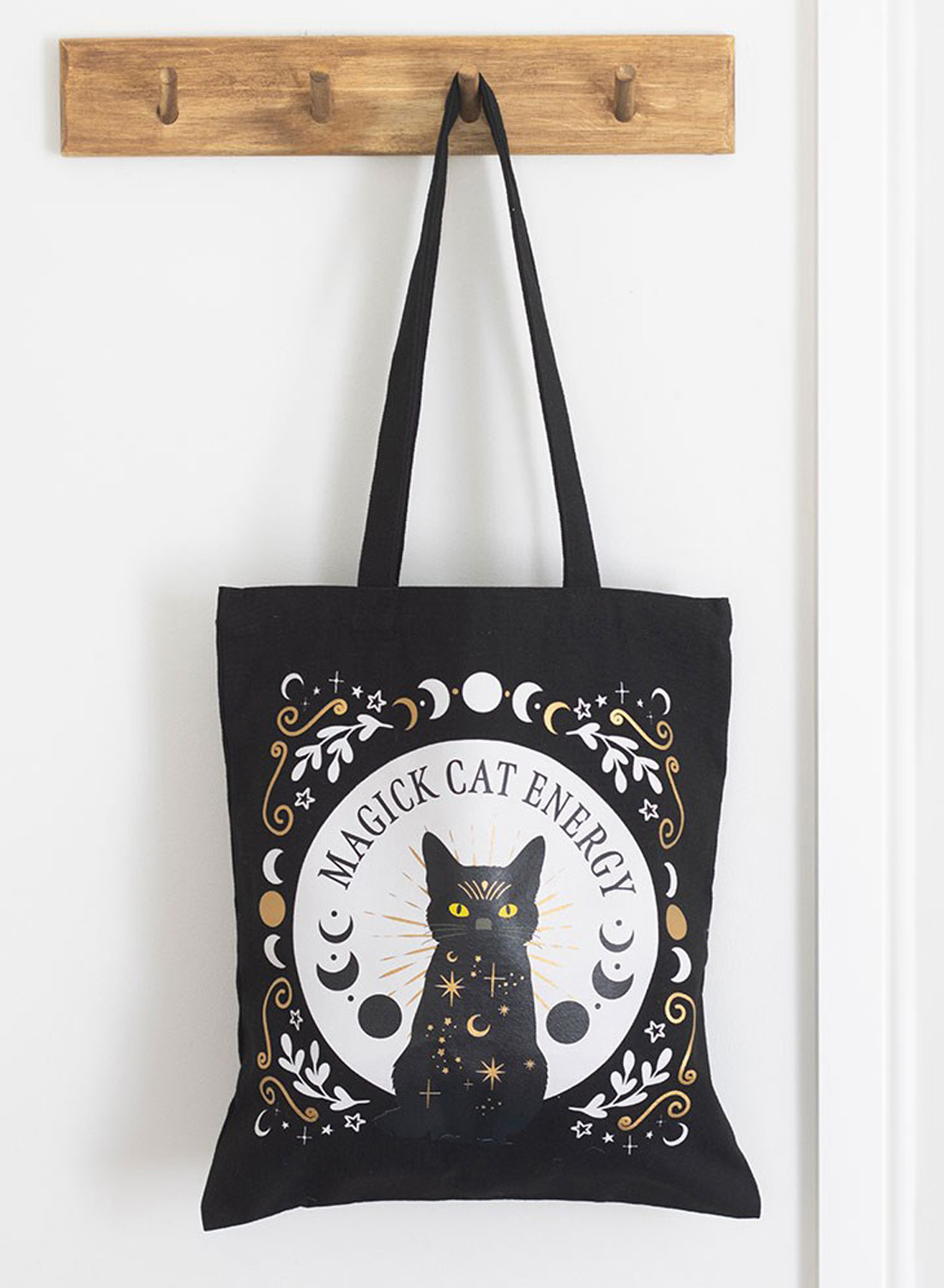 Black Magick Cat Energy Tote Bag – svart tygväska i polyester med kattmotiv, gula ögon, månfaser och stjärnor. Mått 38,5 × 33,8 cm.